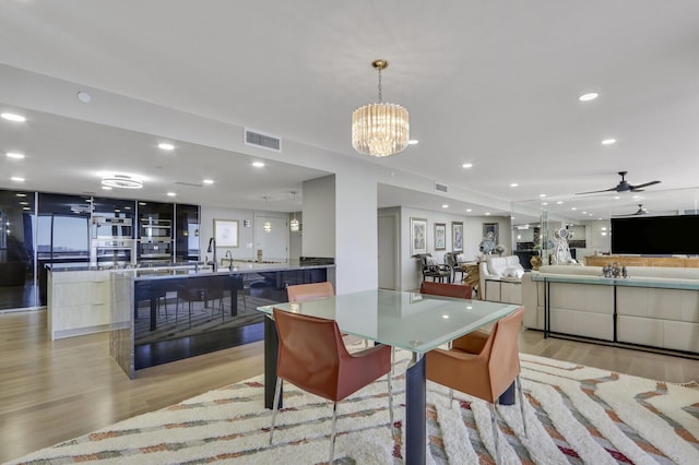 dining room with ceiling fan with notable chandelier and light wood-type flooring