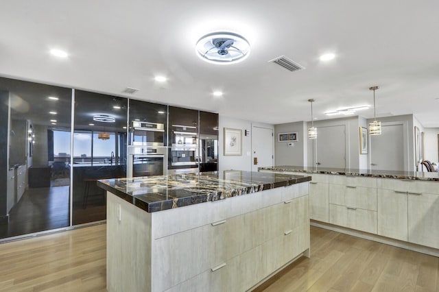 kitchen featuring stainless steel double oven, pendant lighting, a spacious island, and light wood-type flooring