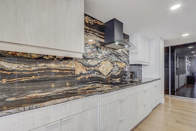 kitchen with white cabinetry, black electric stovetop, island range hood, light hardwood / wood-style floors, and dark stone counters