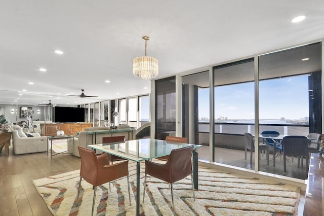 dining area with ceiling fan with notable chandelier, a wall of windows, and light hardwood / wood-style floors