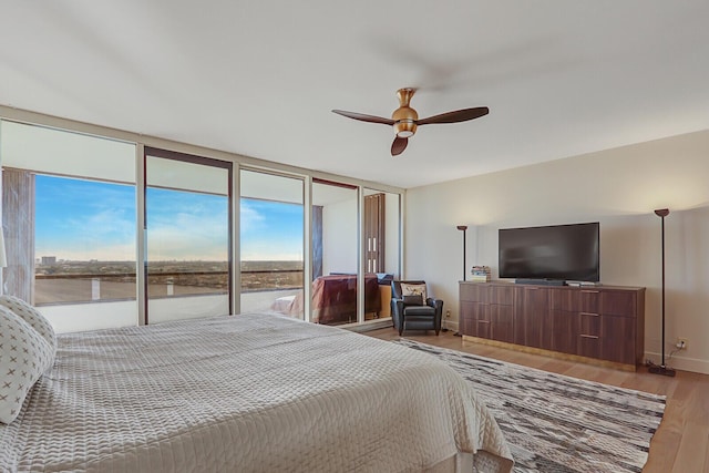 bedroom featuring hardwood / wood-style flooring, a wall of windows, ceiling fan, access to exterior, and a water view