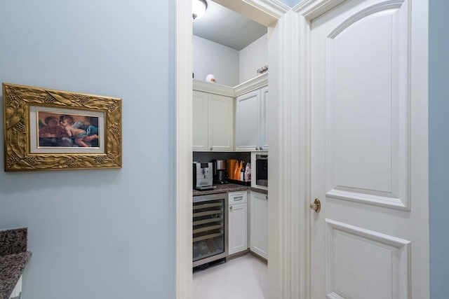 interior space with white cabinetry, dark stone countertops, beverage cooler, and light tile patterned floors