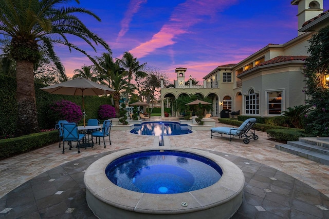 pool at dusk featuring an in ground hot tub and a patio area