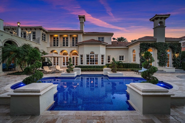 back house at dusk with a patio and a balcony