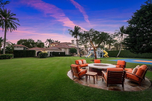 yard at dusk featuring a playground, a patio, basketball hoop, and a fire pit