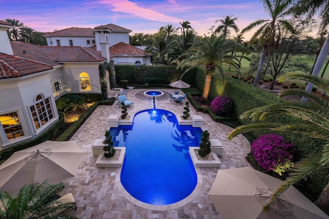 pool at dusk featuring an in ground hot tub and a patio area