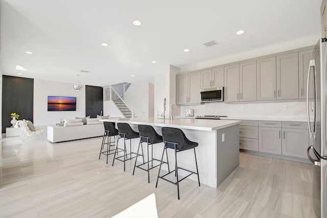 kitchen featuring a breakfast bar area, stainless steel appliances, an island with sink, and gray cabinets