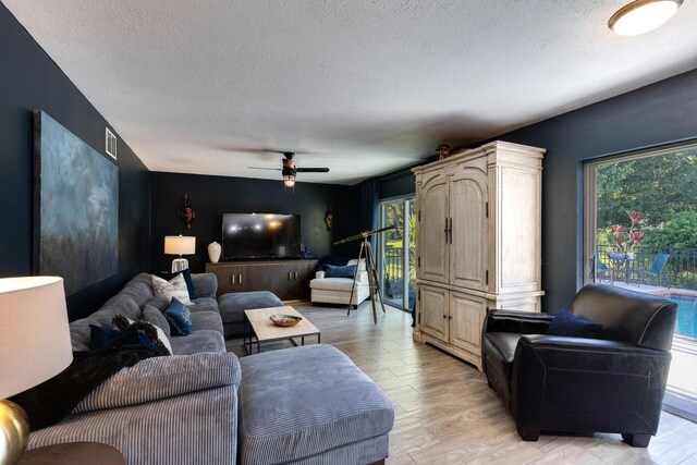 living room with a textured ceiling, light hardwood / wood-style floors, and ceiling fan