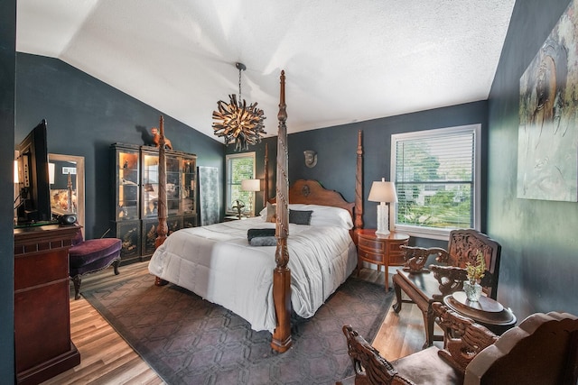 bedroom featuring lofted ceiling, hardwood / wood-style floors, a textured ceiling, and an inviting chandelier