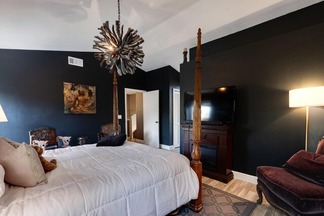 bedroom with hardwood / wood-style flooring, an inviting chandelier, and vaulted ceiling