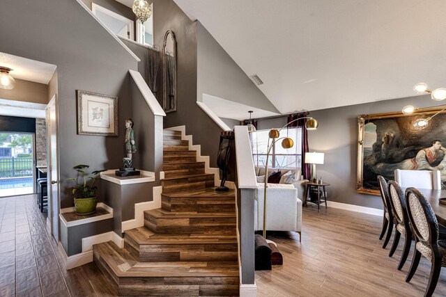 entryway with an inviting chandelier, wood-type flooring, and vaulted ceiling