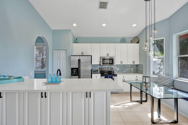 kitchen with appliances with stainless steel finishes, light stone counters, decorative backsplash, light tile patterned flooring, and decorative light fixtures