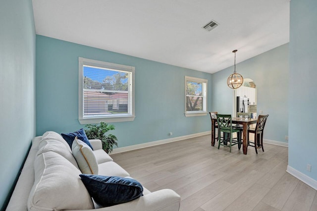 living room with an inviting chandelier, vaulted ceiling, and light wood-type flooring