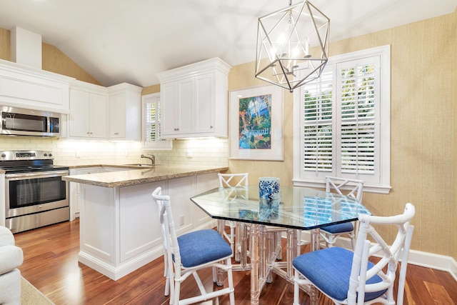 kitchen featuring stainless steel appliances, light stone counters, white cabinets, decorative light fixtures, and vaulted ceiling