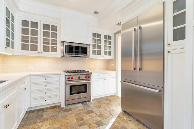 kitchen featuring tasteful backsplash, premium appliances, ornamental molding, and white cabinets