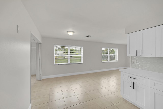 interior space featuring light tile patterned flooring, light stone countertops, decorative backsplash, and white cabinets