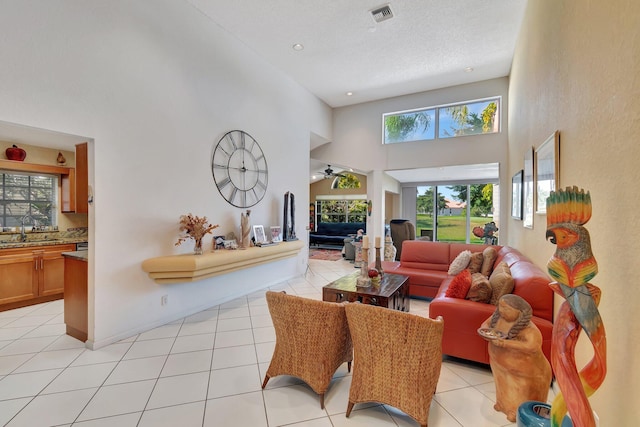 tiled living room with ceiling fan, a towering ceiling, sink, and a textured ceiling