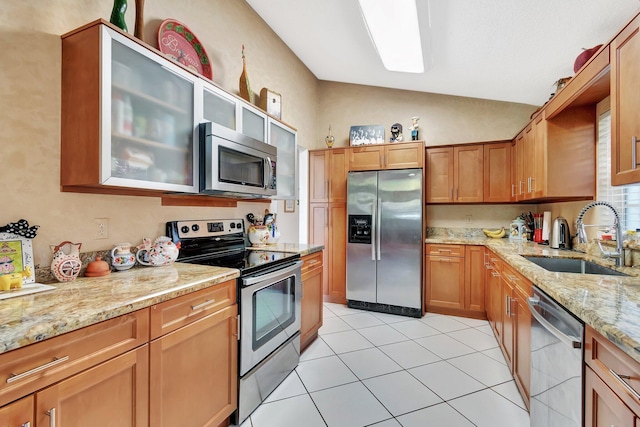 kitchen featuring lofted ceiling, appliances with stainless steel finishes, light stone countertops, and sink