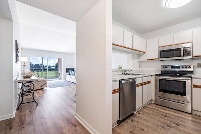 kitchen with lofted ceiling, sink, appliances with stainless steel finishes, light hardwood / wood-style floors, and white cabinets