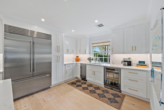 kitchen featuring ornamental molding, beverage cooler, white cabinets, and appliances with stainless steel finishes