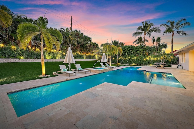 pool at dusk with a patio area, a lawn, pool water feature, and an in ground hot tub