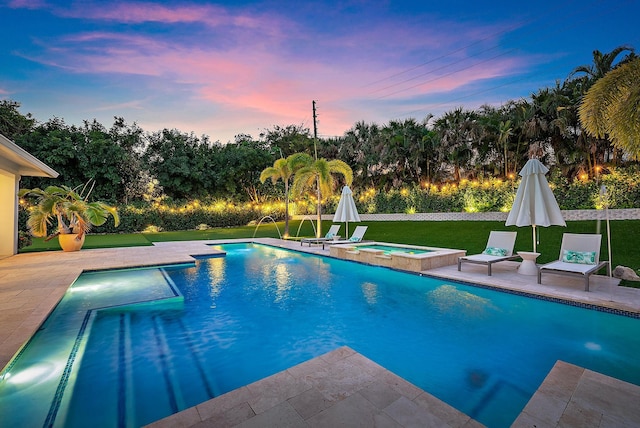 pool at dusk featuring an in ground hot tub, pool water feature, a lawn, and a patio area