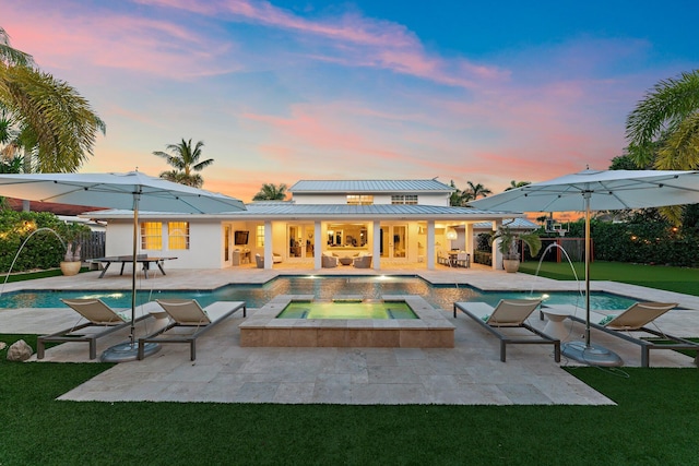 pool at dusk featuring an in ground hot tub, pool water feature, a yard, and a patio