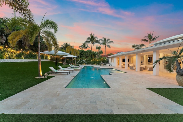 pool at dusk with a patio, a lawn, outdoor lounge area, and pool water feature