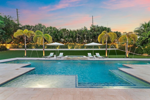 pool at dusk with a patio, pool water feature, and a lawn