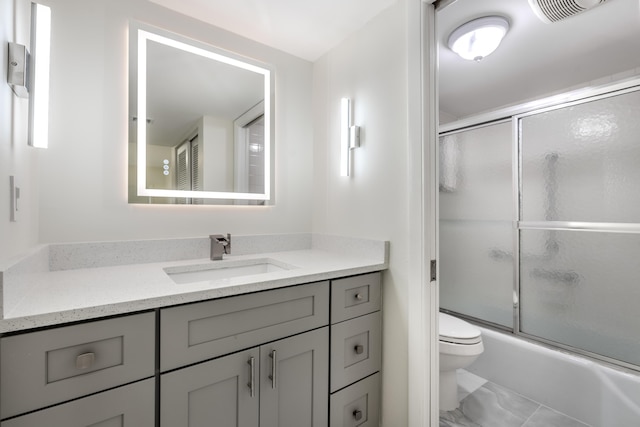 full bathroom featuring vanity, shower / bath combination with glass door, and toilet