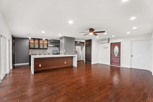 kitchen with an island with sink, an AC wall unit, dark wood-type flooring, and wall chimney exhaust hood