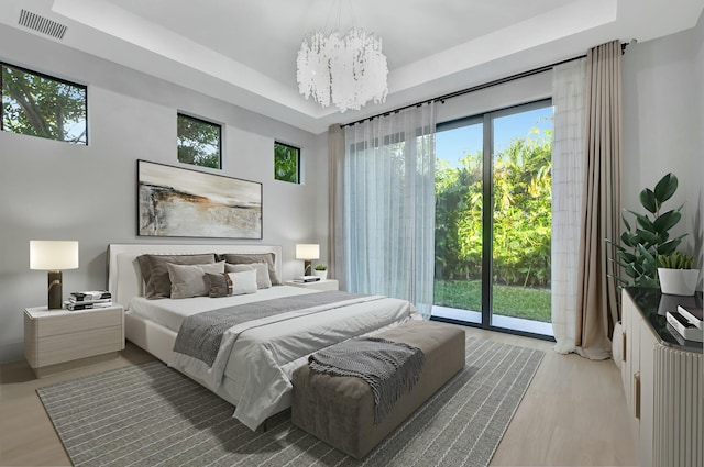 bedroom featuring multiple windows, a tray ceiling, access to exterior, and light hardwood / wood-style flooring