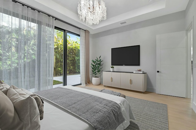 bedroom with a raised ceiling, access to exterior, a notable chandelier, and light hardwood / wood-style flooring