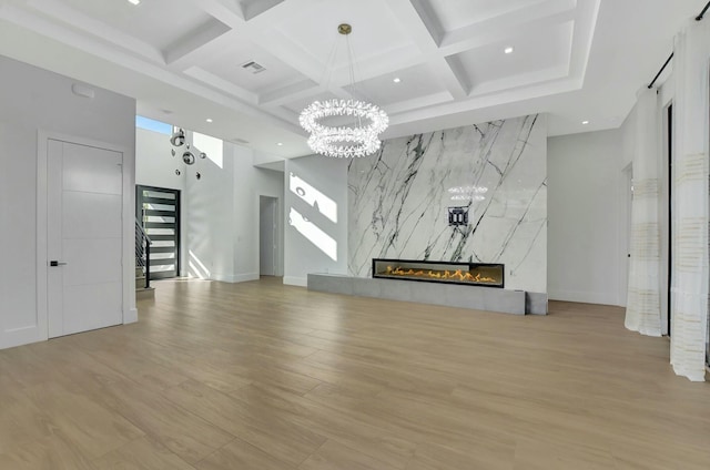 unfurnished living room with coffered ceiling, a premium fireplace, light hardwood / wood-style floors, and beam ceiling