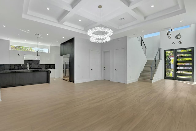 living room featuring coffered ceiling, a towering ceiling, light hardwood / wood-style floors, and a chandelier