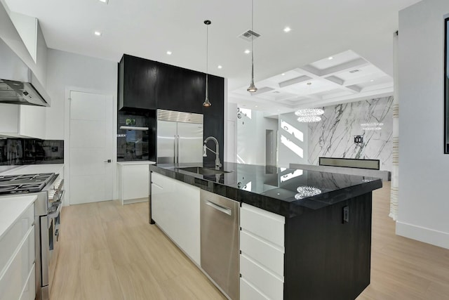 kitchen featuring wall chimney range hood, high quality appliances, coffered ceiling, white cabinets, and a large island with sink