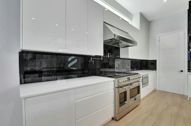 kitchen featuring white cabinetry, stainless steel appliances, tasteful backsplash, wall chimney exhaust hood, and light wood-type flooring