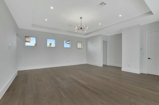 spare room with dark hardwood / wood-style flooring, a raised ceiling, and an inviting chandelier