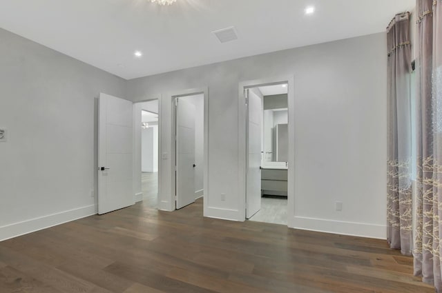 unfurnished bedroom featuring ensuite bath, a walk in closet, and dark hardwood / wood-style floors