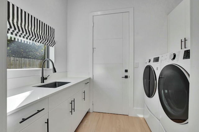 clothes washing area with sink, cabinets, washing machine and clothes dryer, and light wood-type flooring