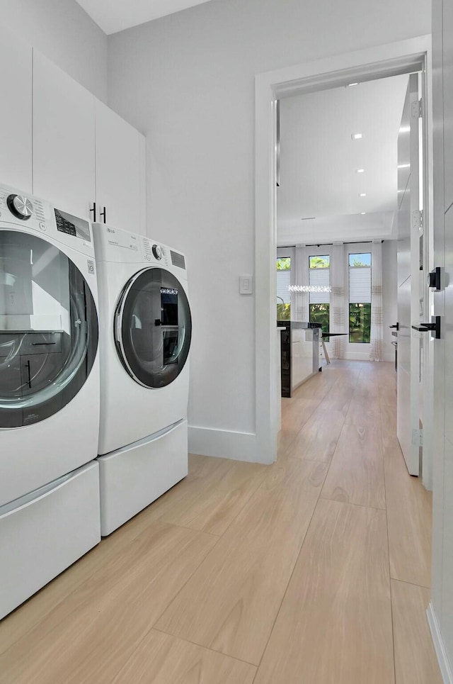 washroom with cabinets, washer and dryer, and light hardwood / wood-style flooring