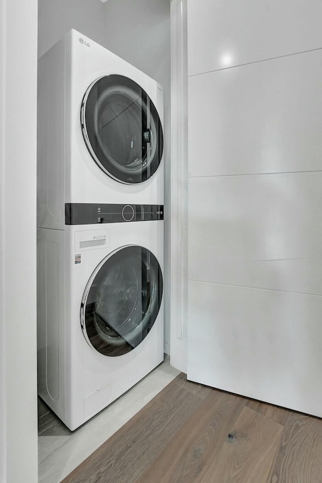 laundry room with hardwood / wood-style flooring and stacked washer / dryer