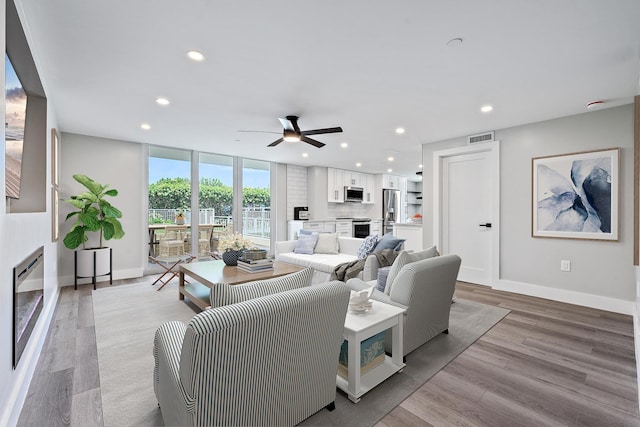 living room featuring floor to ceiling windows, ceiling fan, and light wood-type flooring