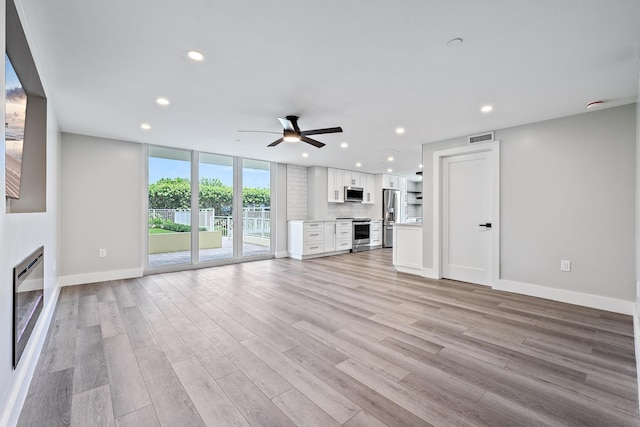 unfurnished living room featuring a wall of windows, ceiling fan, and light wood-type flooring