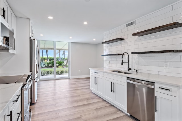 kitchen with light stone countertops, white cabinetry, appliances with stainless steel finishes, and sink