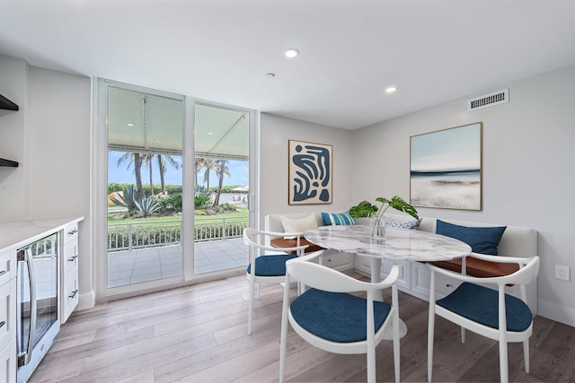 dining space featuring breakfast area, expansive windows, light hardwood / wood-style flooring, and wine cooler