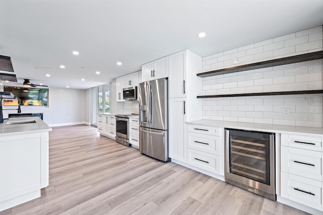 kitchen featuring appliances with stainless steel finishes, backsplash, wine cooler, white cabinets, and light wood-type flooring