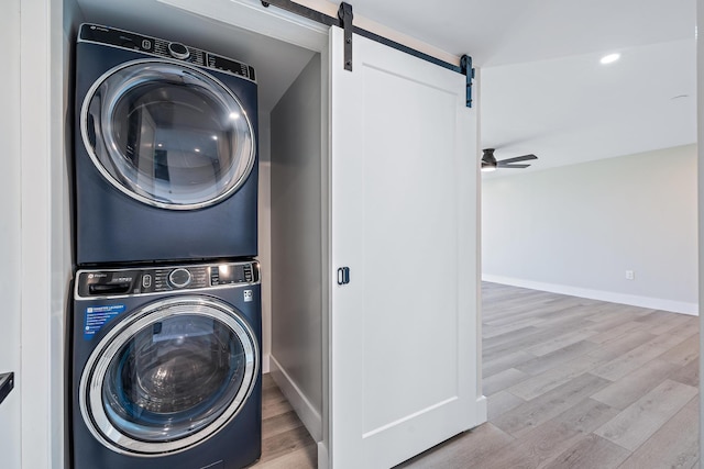 clothes washing area featuring ceiling fan, a barn door, stacked washer / drying machine, and light hardwood / wood-style floors