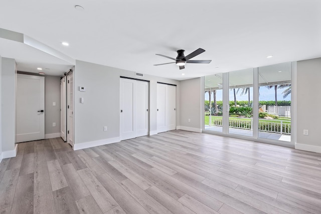 unfurnished room with expansive windows, ceiling fan, a barn door, and light hardwood / wood-style floors