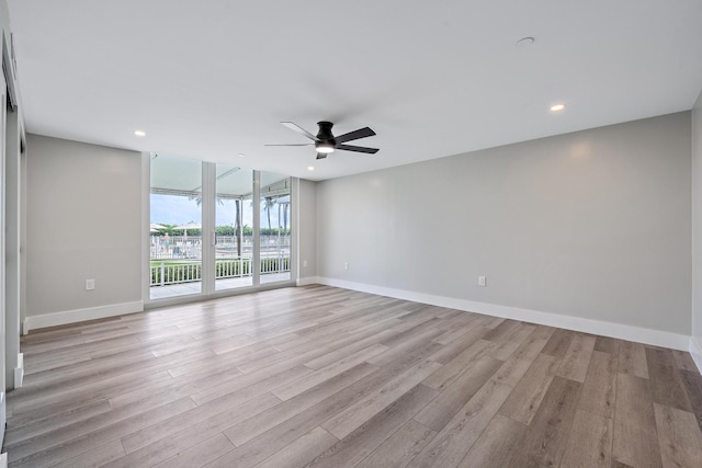 spare room with ceiling fan, a wall of windows, and light hardwood / wood-style floors